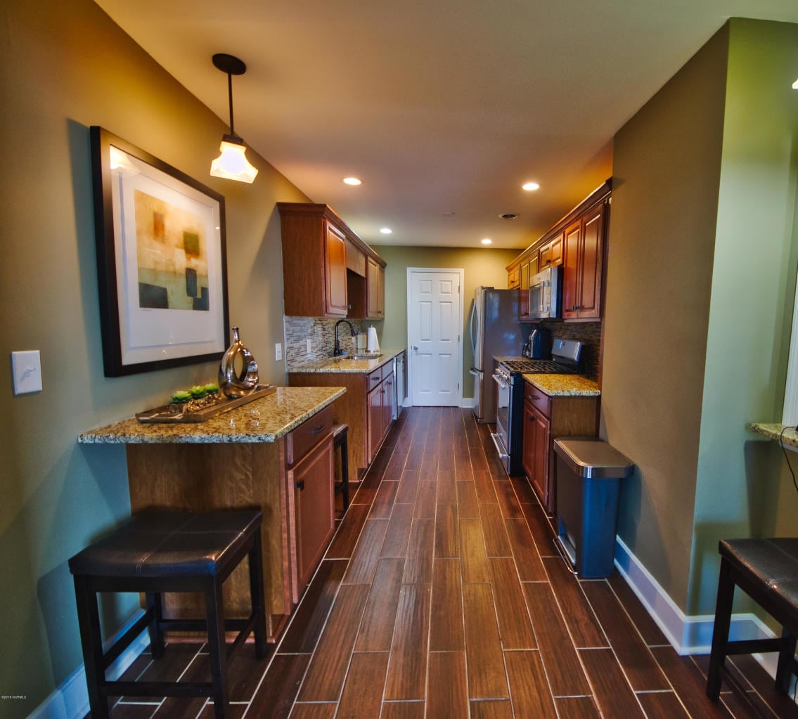 The kitchen features dark wood cabinetry, granite countertops, and modern appliances, providing a functional space for meal preparation. A breakfast bar with seating for two is included. Warm lighting casts a welcoming glow over the area, complemented by natural light from the window.