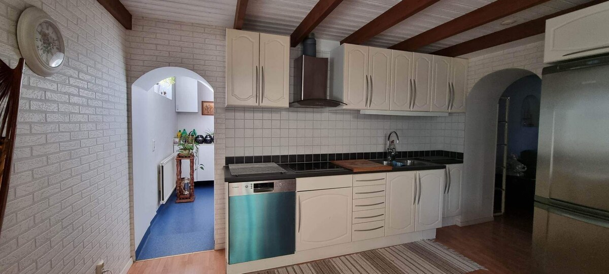 A spacious kitchen with modern appliances is featured, including a stainless steel dishwasher and an oven. Light-colored cabinetry complements the black countertops. A doorway leads to a well-lit adjacent area, creating an open and inviting layout.