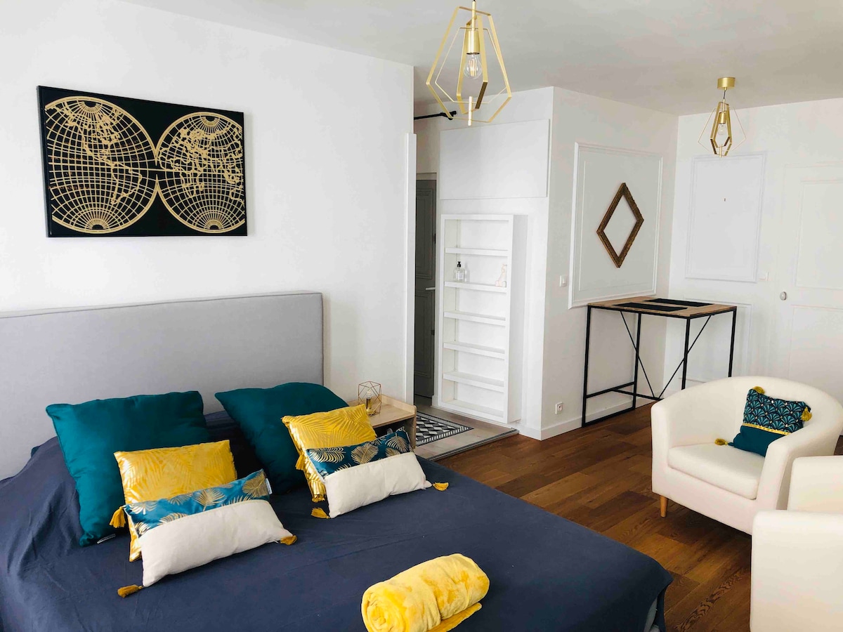 A spacious sleeping area features a comfortable bed adorned with colorful pillows and a soft throw. An accent wall decorates the room with a world map artwork. Nearby, a cozy armchair and a minimalist table are visible against a bright, neutral backdrop.