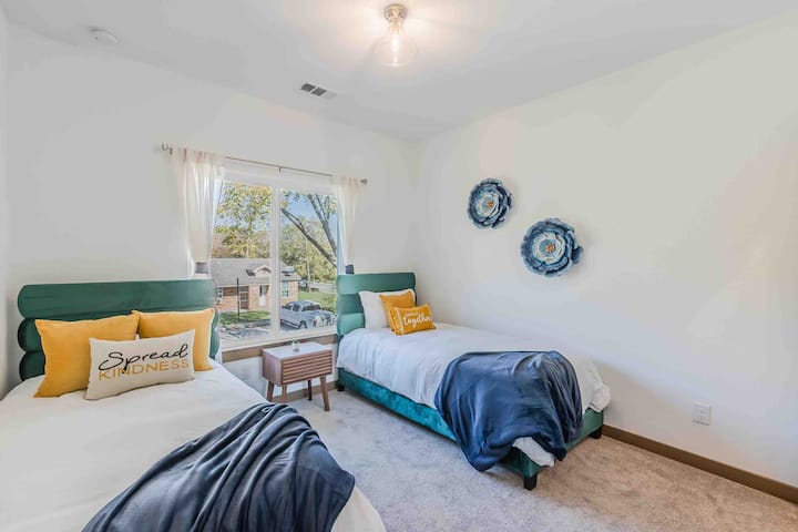 Chumba cha kulala cha tatu chenye nafasi kubwa chenye vitanda viwili vya kisasa lakini vyenye starehe. Meza janja iliyowekwa katika b/w. Chumba hicho kimewekwa zulia na kina dirisha kubwa ambalo huipa sehemu nzima mandhari safi na yenye kuvutia.  