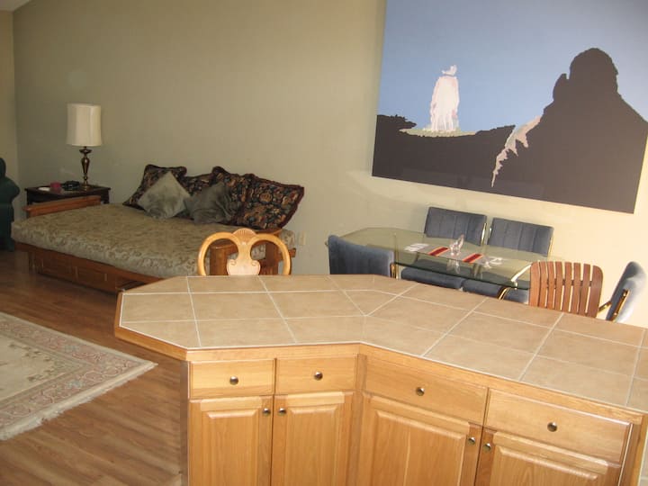 Part of the living room area with futon with ( springs ) in sleeping or down position . Some of the dining and island from the kitchen also is in display .