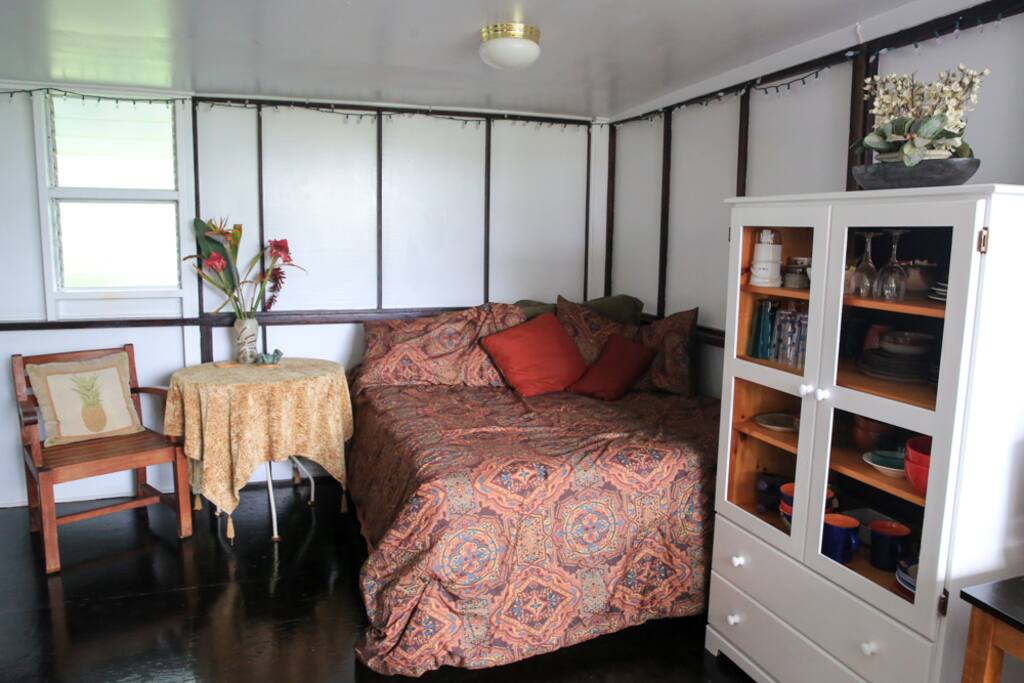 King bed with lots of pillows and hutch with kitchen utensils.