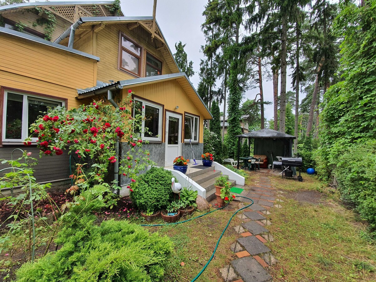 The exterior of the cottage showcases a welcoming garden area with vibrant flowers. Stone paths lead to the entrance, and seating is arranged under a covered area. Lush trees surround the property, creating a private and serene atmosphere.