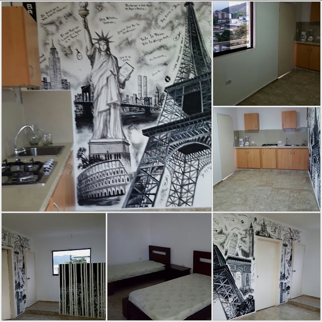 The studio apartment features a compact kitchen area with essential appliances and a dining space. Distinctive wall art depicting iconic landmarks adds visual interest, while a bright window provides natural light. Two spacious beds are positioned along the opposite wall, enhancing the sleeping area.