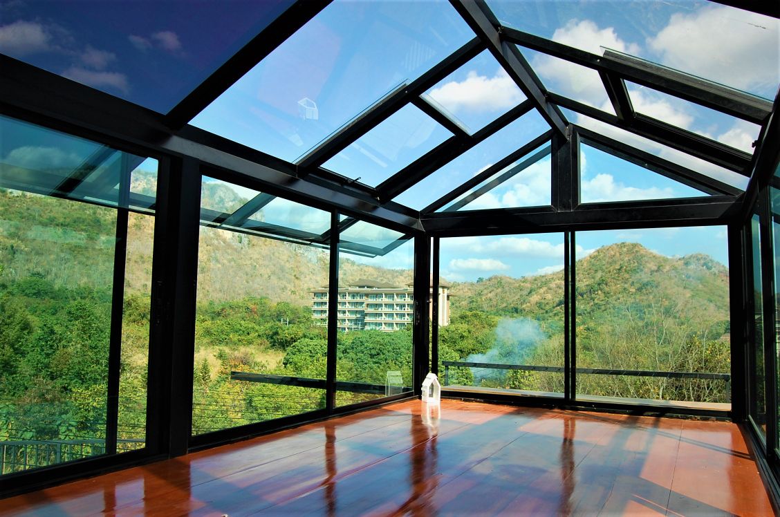 A glass-enclosed space features large windows that offer views of the surrounding mountains and greenery. The wooden floor enhances the sense of openness, and a lantern is placed in one corner, adding a subtle decorative element to the serene environment.