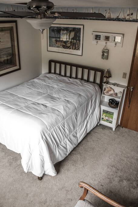 Guest room with comfy queen bed, ceiling fan, and clean carpet.