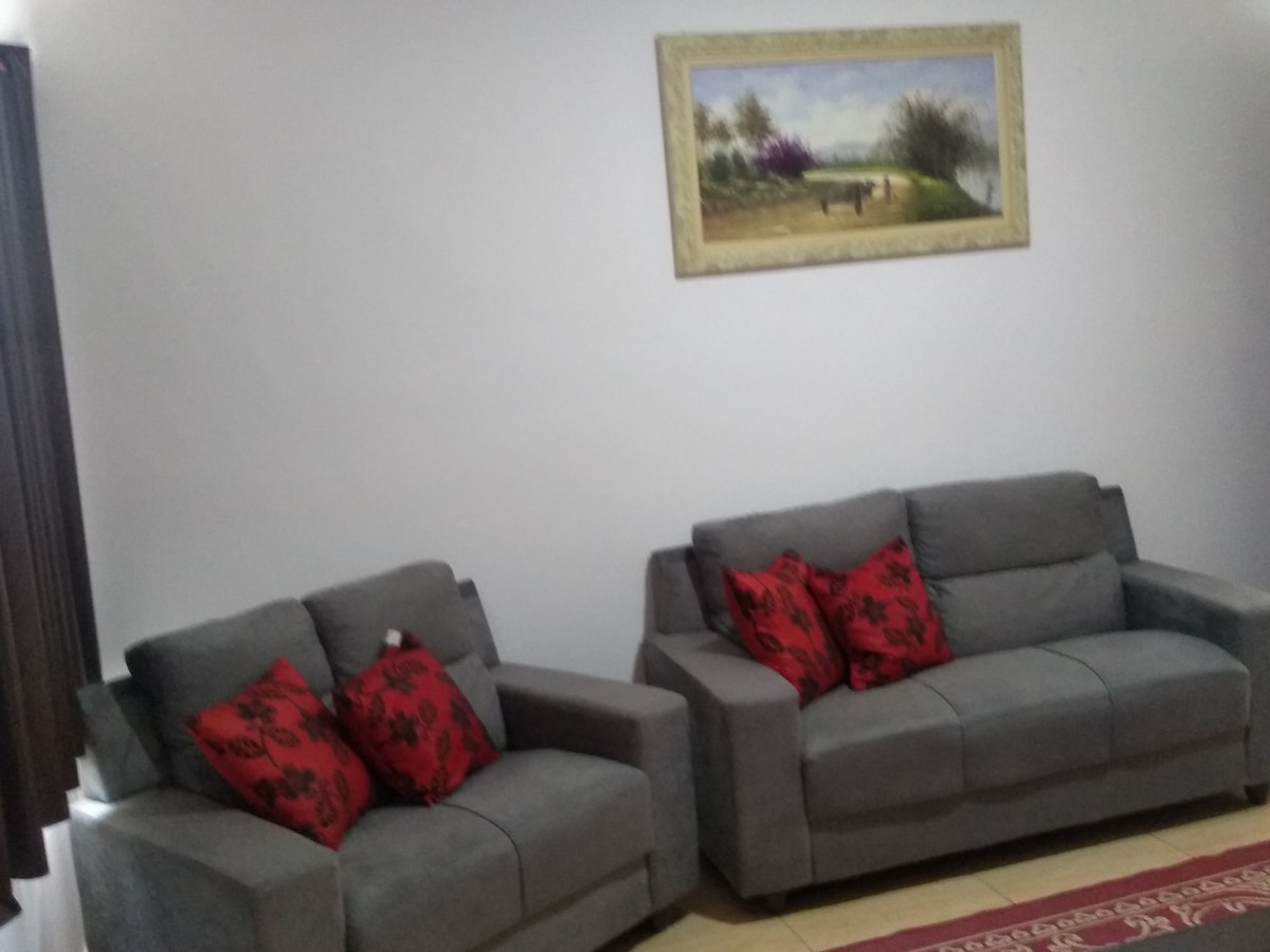 Two gray sofas with decorative red and black cushions are positioned against a light-colored wall. A framed landscape painting adorns the wall above the sofas, adding a touch of color to the space.
