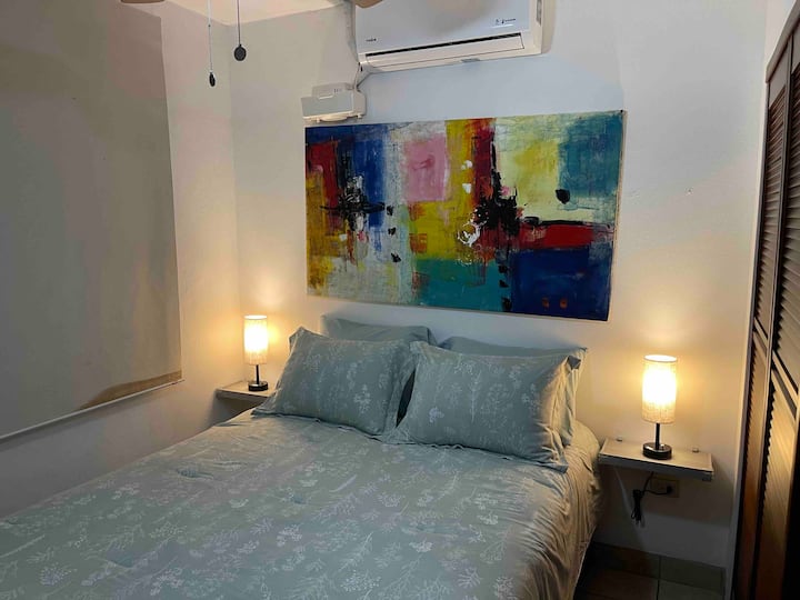 Master BR con una cama tamaño queen, mesitas de noche con protectores de esquina, lámparas regulables con 110V, conectores USB y USB-C para tu comodidad. Armario empotrado con perchas. Almohada y manta adicionales en el interior del armario. Aire acondicionado y ventilador de techo.