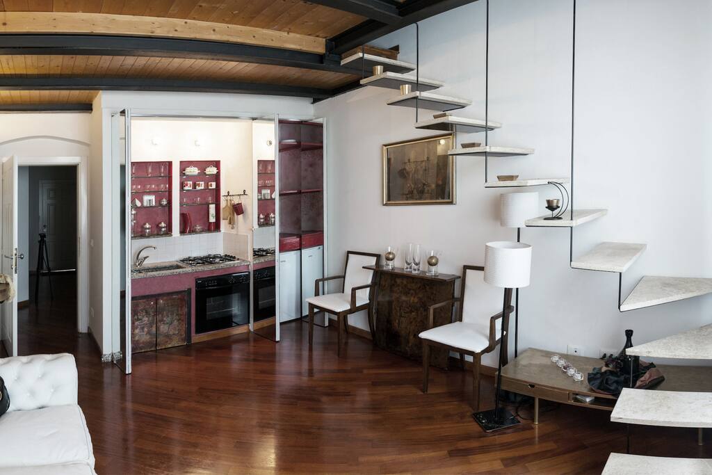Piano primo, cucina attrezzata in muratura e dispensa a scomparsa dentro grande specchiera. Tavolo da pranzo a scomparsa tra le due poltroncine in pelle e legno.
