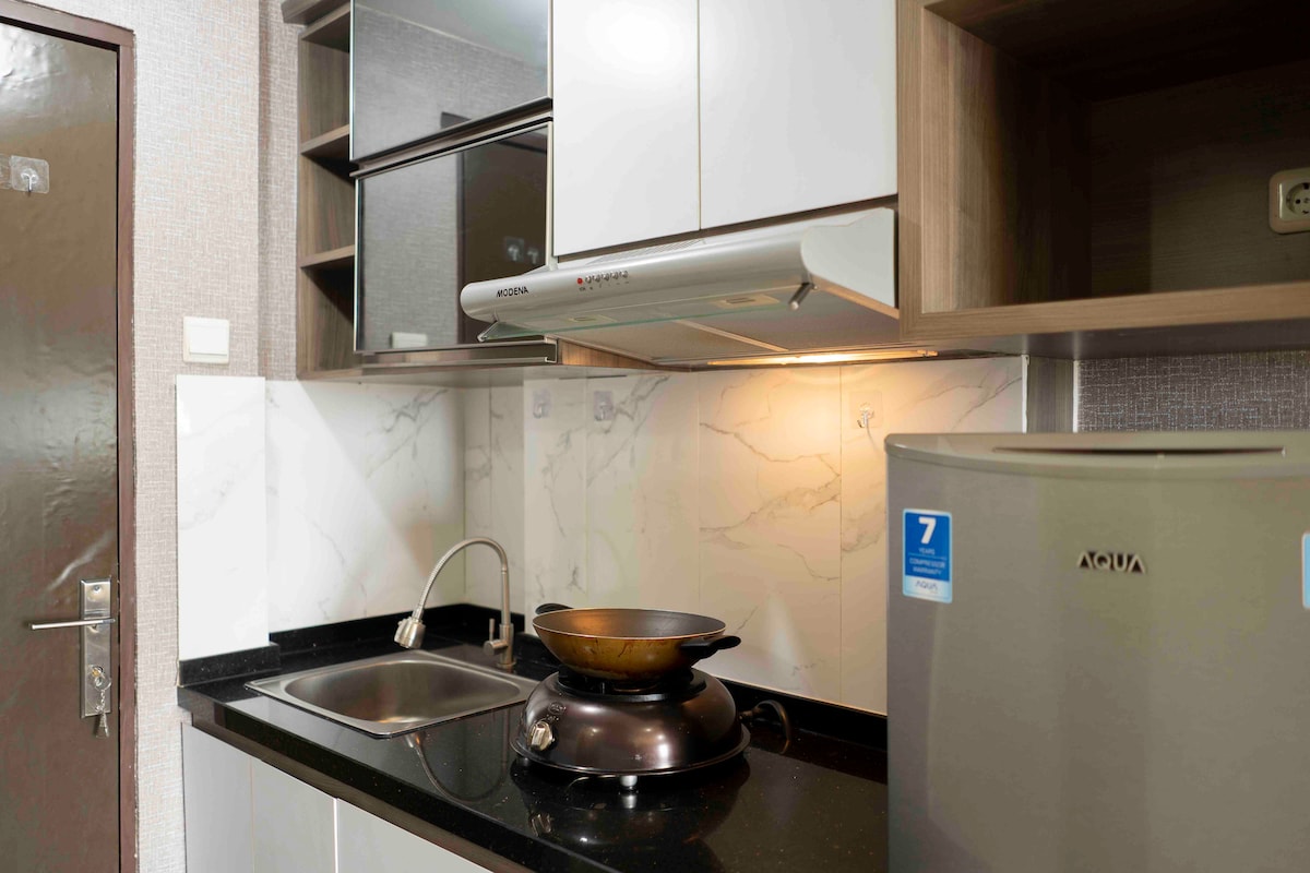 A functional kitchenette featuring a sleek black countertop and a stainless steel sink. Upper cabinets provide storage space, while a small refrigerator sits to the right. An induction stove is positioned on the counter, complemented by a modern hood above for ventilation.