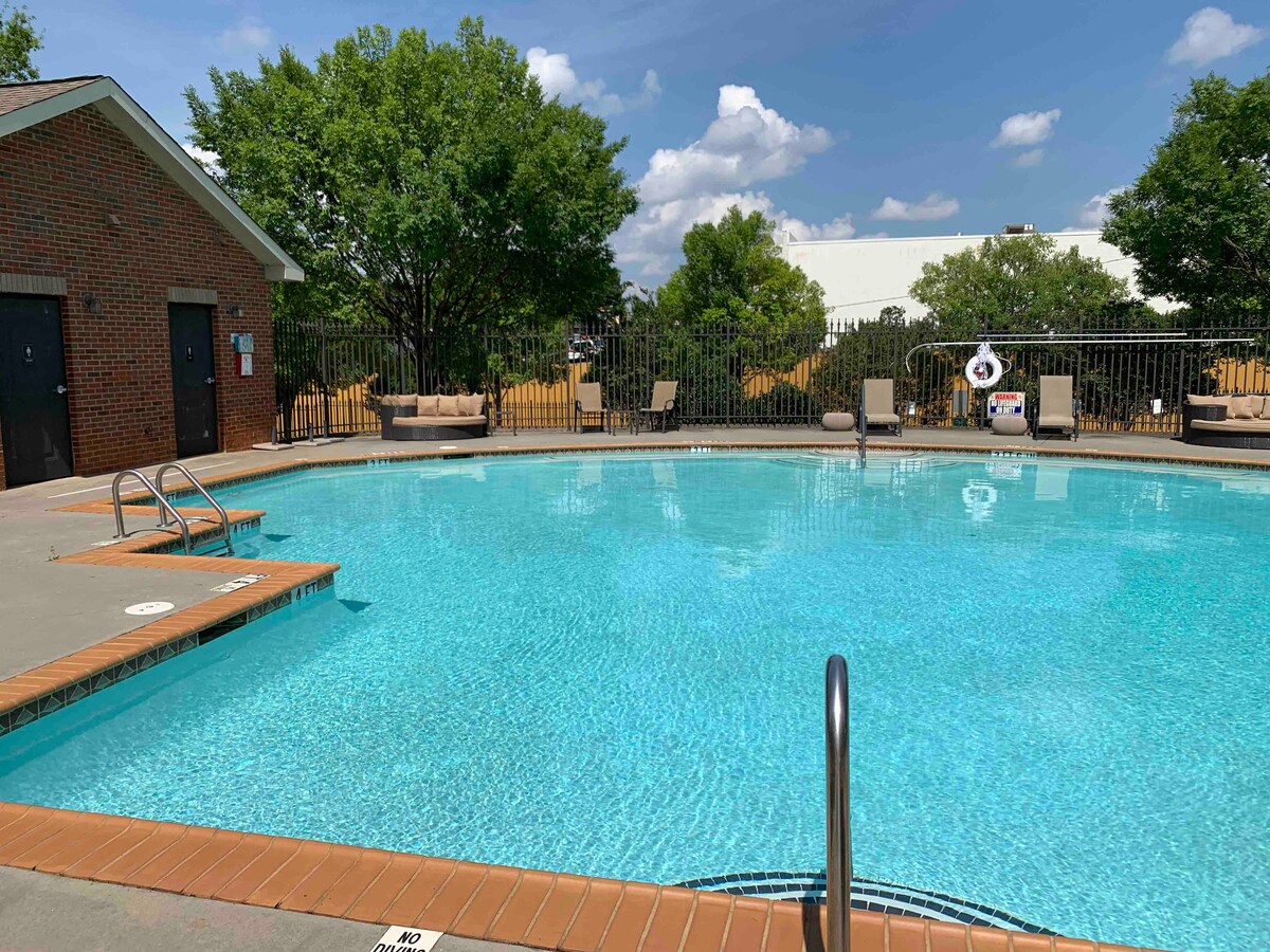 A clear and inviting swimming pool is surrounded by a landscaped area. Comfortable lounge chairs are placed along the poolside, providing a space for relaxation. Lush trees offer shade, enhancing the tranquil setting for guests.