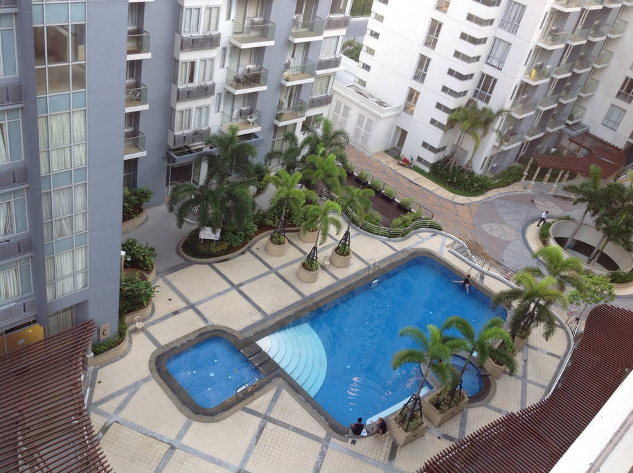 An aerial view showcases a swimming pool surrounded by well-maintained landscaping. Palm trees add greenery to the area, while the pool's clear blue water invites relaxation. The surrounding buildings feature balconies, creating an interconnected community atmosphere.