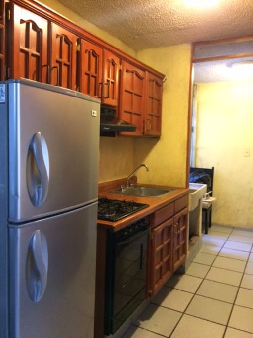 Cocina Integral con refrigerador, horno de microondas, vajilla, cubiertos y accesorios para cocinar.
