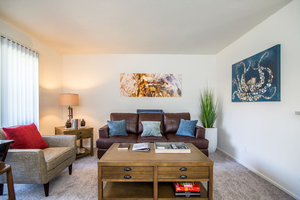 Living room with modern glass artwork, sleeper sofa, and coffee table equipped with coasters, board games, extra throw pillows, and books for casual reading