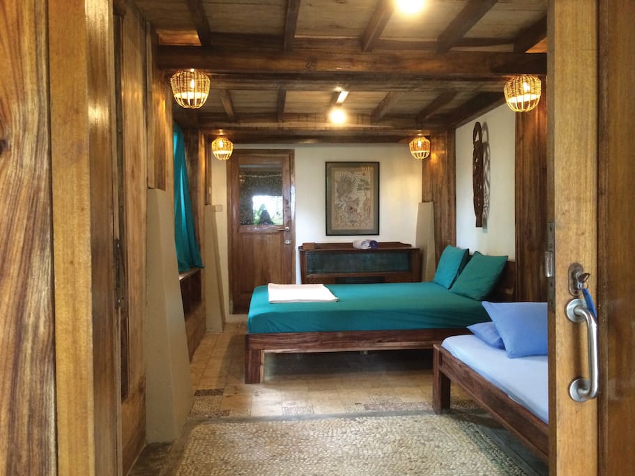 GREEN TRIPLE ROOM (downstairs ~ under the Family Surf Room ~ Ideal for 2 persons) •Bedroom 3x6m2 •1queen size bed with mosquito net •1Single Bed with mosquito net •Verandah 3x3m2, 1 hammock •Bathroom 2x3m2, western standard toilet, cold shower, sink and mirror •Aircond. •In-room safety box •Writing desk •Breakfast for 3 persons