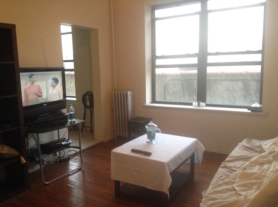 The living room with futon couch/bed, coffee table, tv, and kitchen.