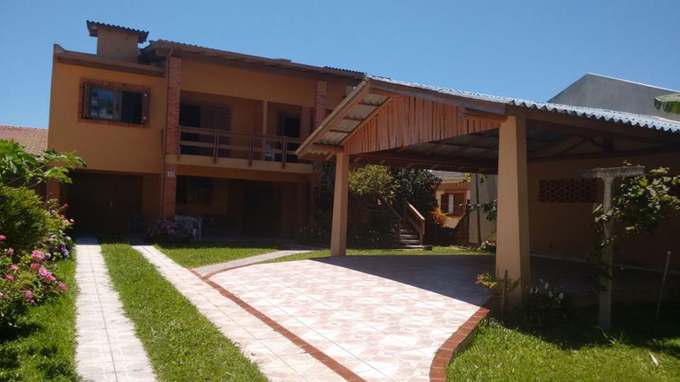 A welcoming exterior of a two-story building is highlighted, featuring a covered parking area and a spacious path lined with vibrant landscaping. The balcony and large windows create an open feel, while the light colors of the walls blend harmoniously with the clear blue sky.