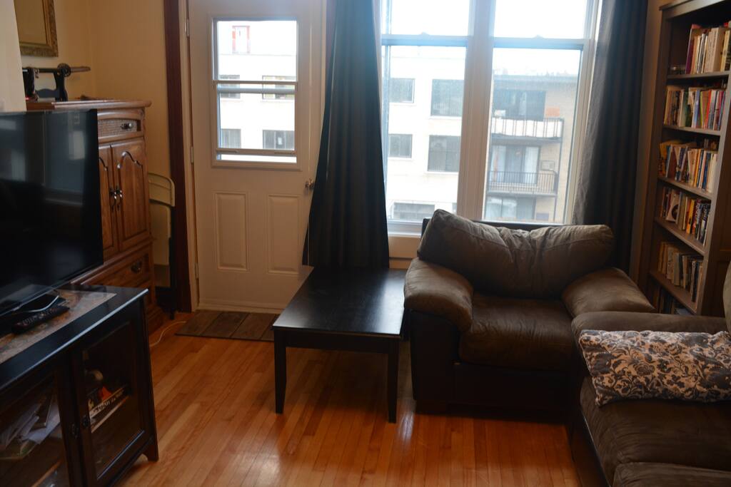 TV Room with front balcony, 2nd bedroom with single-bed sized couch and beddings, plus closed door.