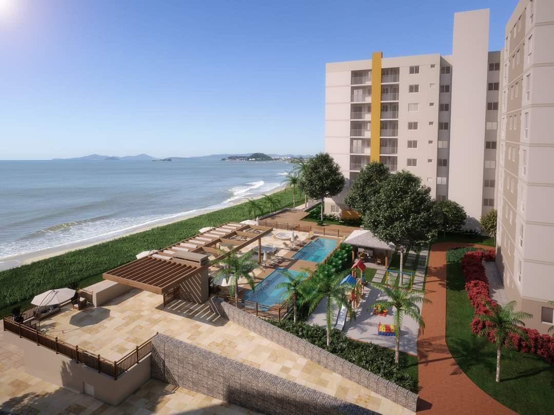 A view of the outdoor area is presented, featuring a swimming pool surrounded by lounge chairs and tropical landscaping. The beach borders the property, while a path leads to the building. The backdrop showcases a clear sky and distant hills along the coastline.