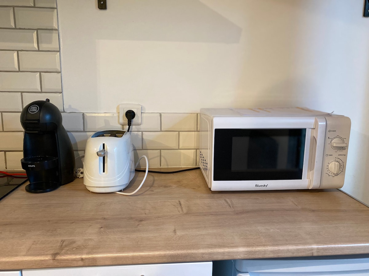 A kitchen countertop features essential appliances, including a coffee maker, a toaster, and a microwave. The surface is made of light-colored wood, complemented by a tiled backsplash in neutral tones, enhancing the functional workspace.