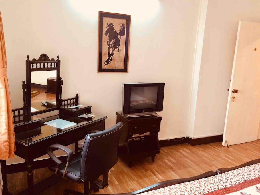 This photograph shows an antique dressing table which can also be used as a writing table / laptop table. A swivel chair for comfort and convenience. A colour TV with a cable connection.