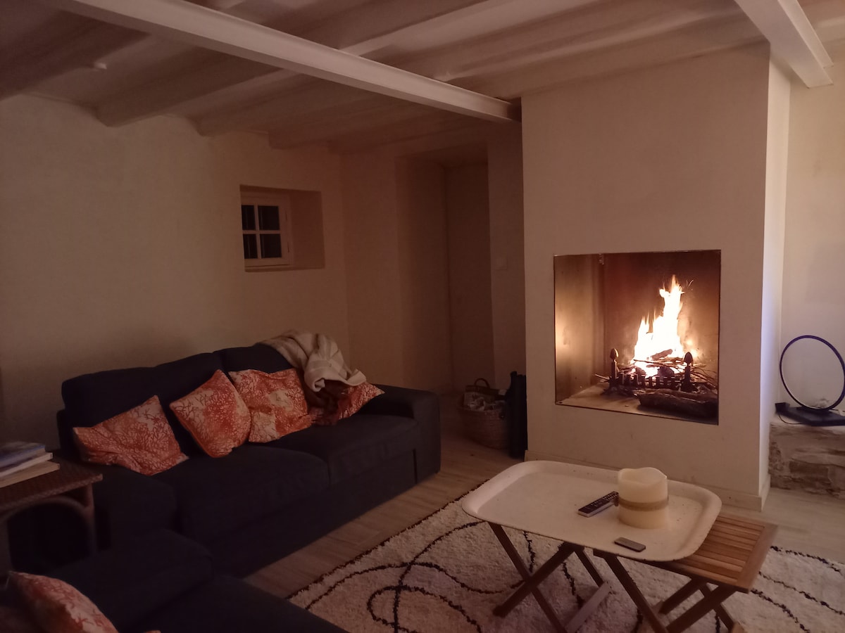 A cozy living area is highlighted by a fireplace, providing warmth and a focal point. A dark sofa with patterned cushions faces a simple coffee table, while soft lighting enhances the inviting atmosphere. The walls are painted in a light shade, creating a serene backdrop.