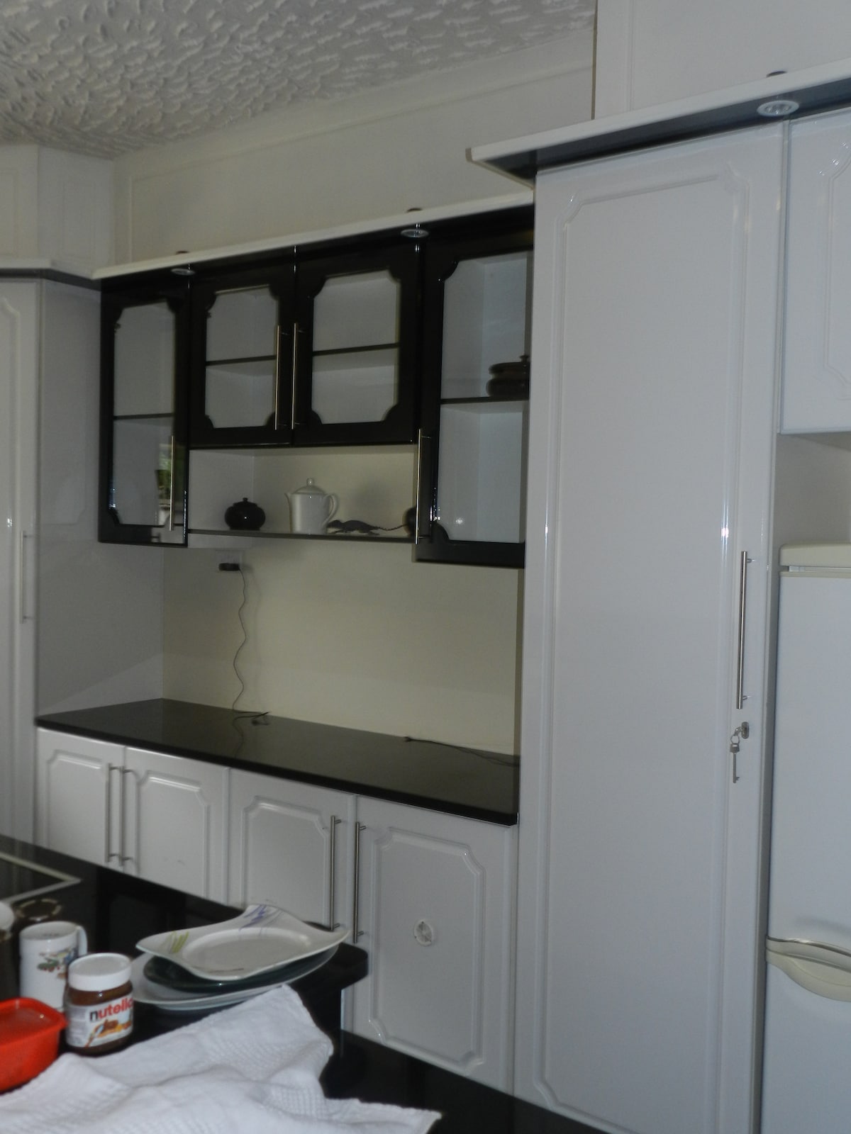 A modern kitchen space is highlighted by sleek black and white cabinetry, featuring glass-fronted upper cabinets. A black countertop extends across the base units, complemented by essential kitchen appliances, creating a functional cooking environment.