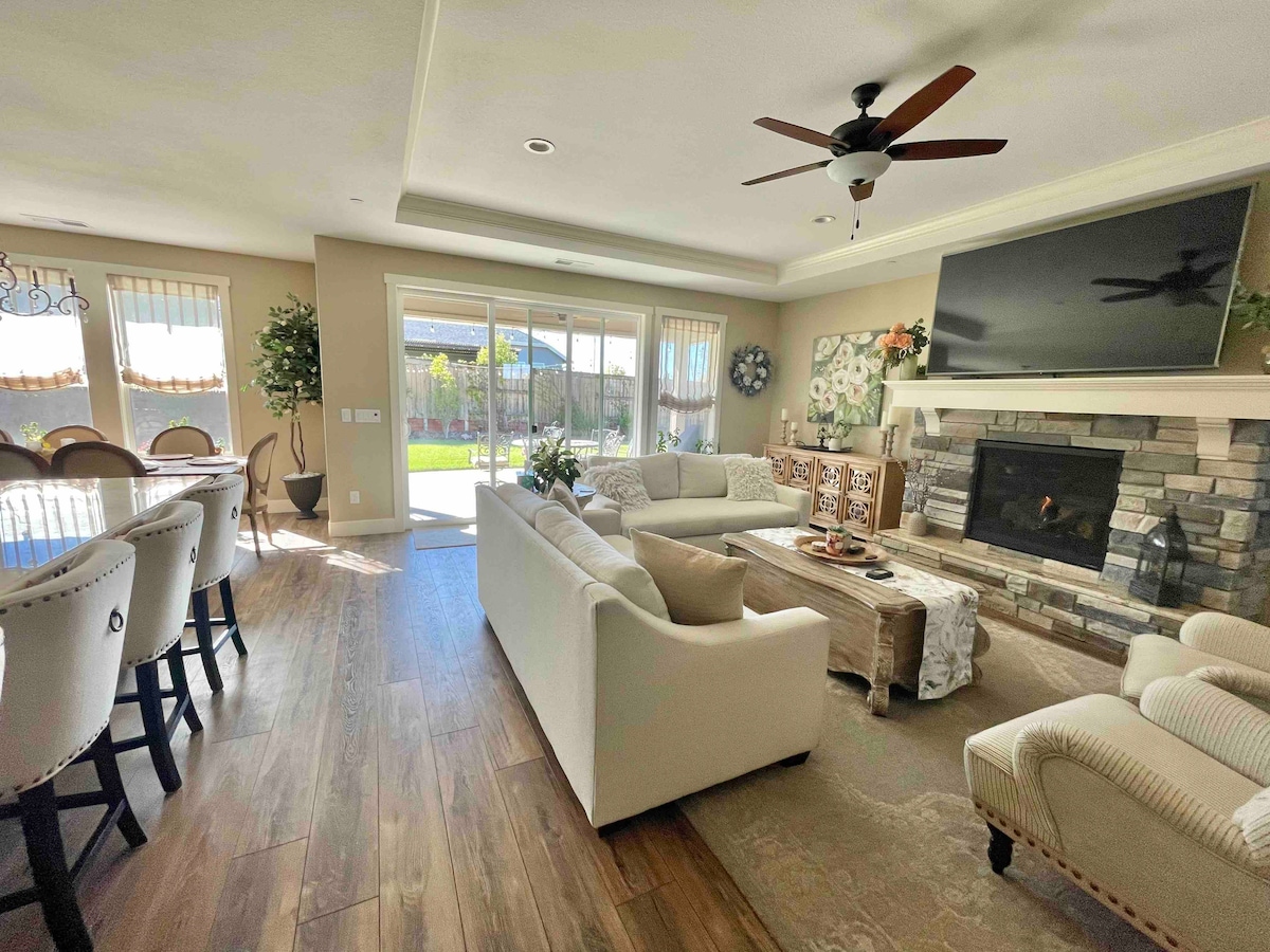 A light-filled living area features comfortable seating arranged around a coffee table. A stone fireplace serves as a focal point, while a large television is mounted on the wall above. Large glass doors lead to a patio, allowing for seamless indoor-outdoor flow.