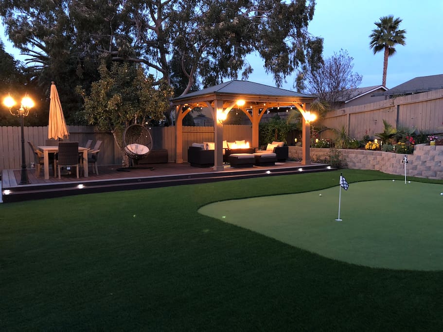 Very peaceful large backyard with putting green, lounge chairs, dining table, deck, and flower garden.