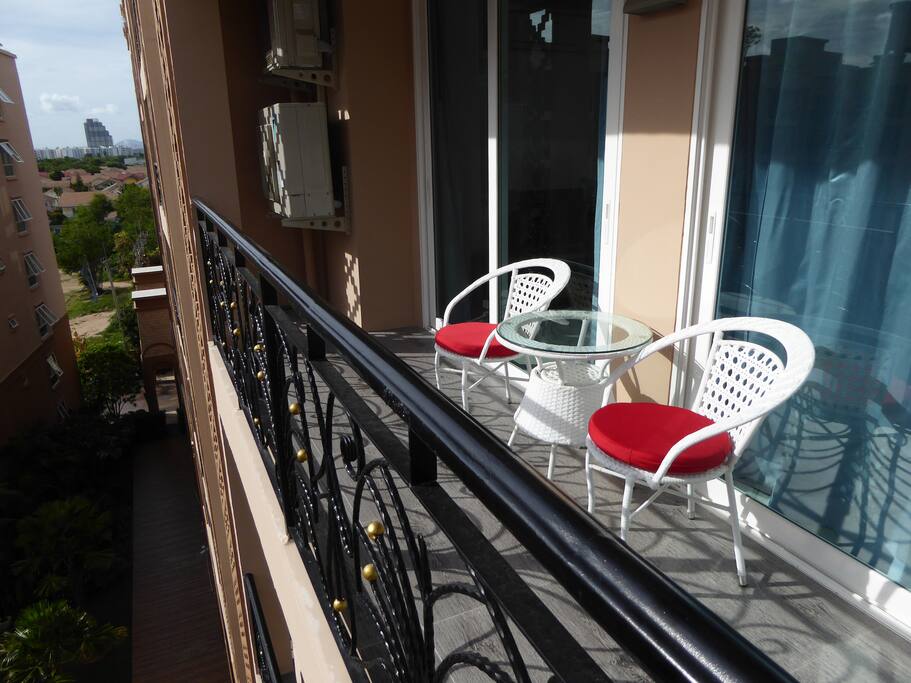 Stylish outdoor table and chairs with cushions on large balcony overlooking pool view