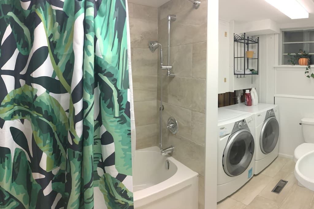 The newly renovated bathroom features a large tub and shower, plentiful space, and shared laundry appliances.