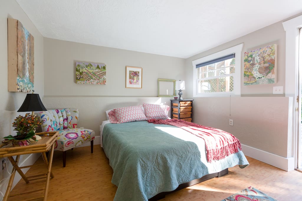 Bedroom features original artwork for sale and gorgeous views from window and door.
