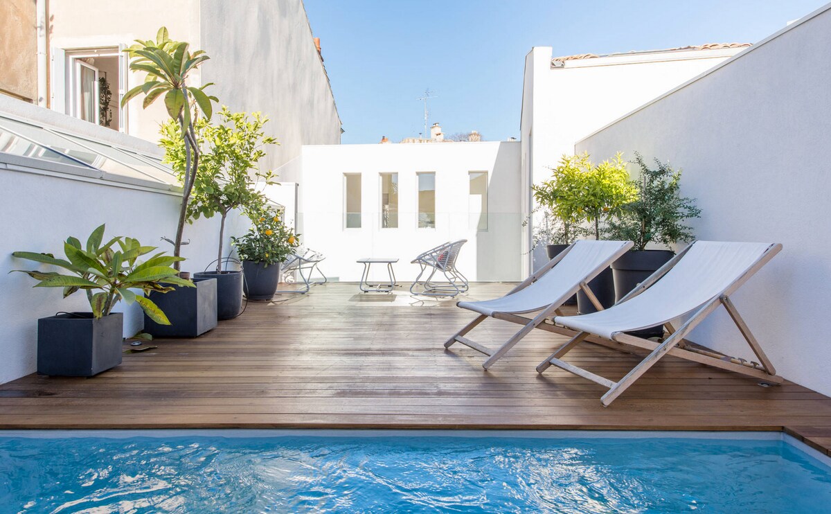 A private rooftop terrace is presented, featuring a small pool surrounded by wooden decking. Relaxing lounge chairs are positioned near potted greenery, creating a tranquil outdoor space. The white walls and natural light enhance the inviting atmosphere of the area.