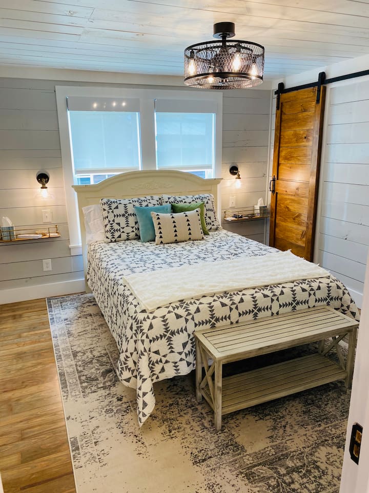 The bedroom has a queen bed with dual blackout/transparent layered shades, a remote controlled fan/light, sliding barn door closet, and light switch controlled bedside lights. 
