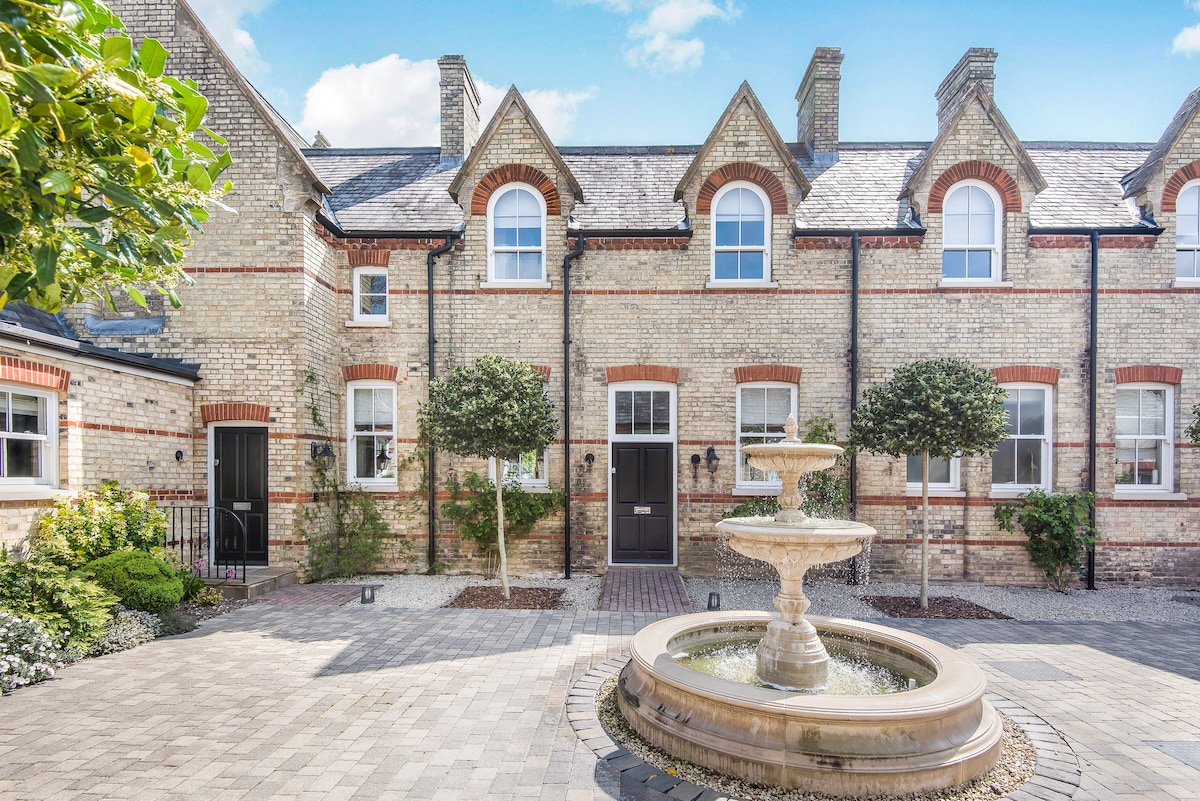 The charming facade of the property is framed by thoughtfully placed trees and neatly trimmed shrubs. A classic stone fountain serves as a focal point in the courtyard, surrounded by cobblestone pathways that enhance the welcoming atmosphere.
