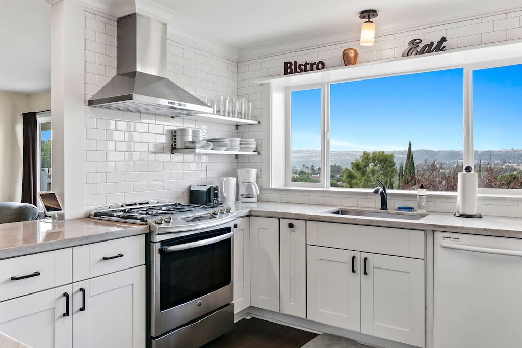 White subway tile and a stainless gas range are on display next to a massive window overlooking California hilltops.