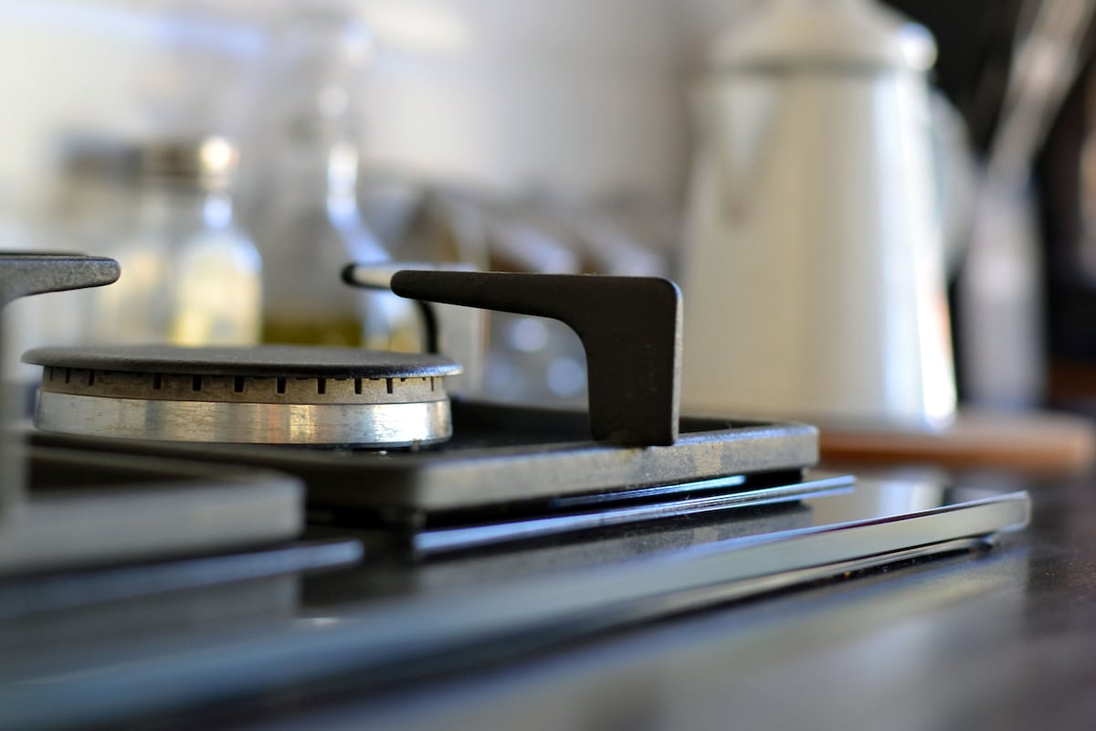 A modern gas stove is prominently displayed on a sleek countertop. The burner features a minimalist design with a metallic finish. Glass jars filled with various ingredients are arranged in the background, while a white kettle is softly illuminated to the side.