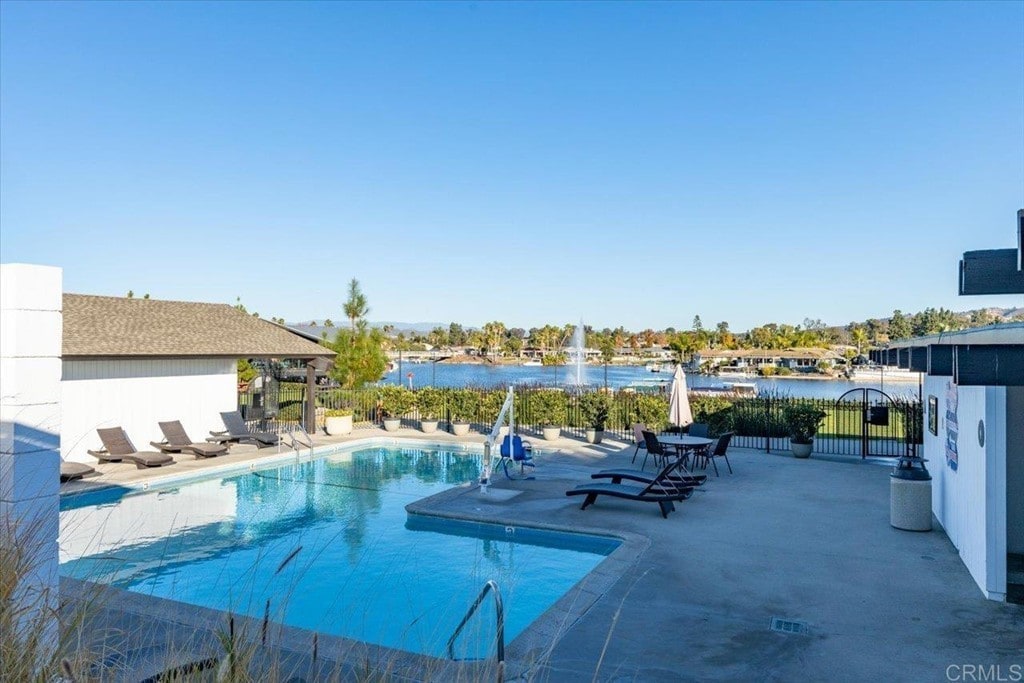 A serene outdoor pool area is displayed, featuring comfortable lounge chairs arranged around the poolside. The water glistens under clear blue skies, with views of the adjacent lake and palm trees in the background, creating a peaceful atmosphere.