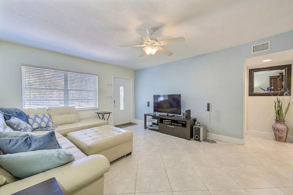 The living room is furnished with an upscale white leather sectional and ottoman. Sink into ocean-blue pillows and watch your favorite films on the 52” flat-screen TV.