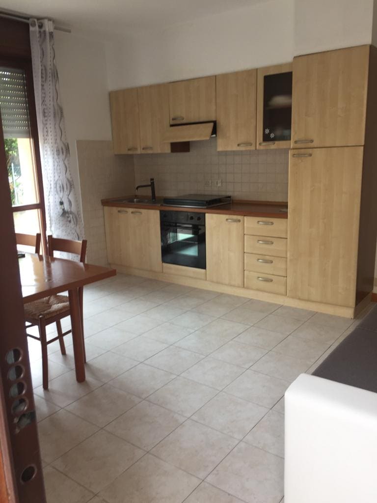 A functional kitchen area is equipped with wooden cabinetry and essential appliances, including an oven and a stovetop. A small dining table with four wooden chairs is positioned nearby, while large windows allow natural light to brighten the space.