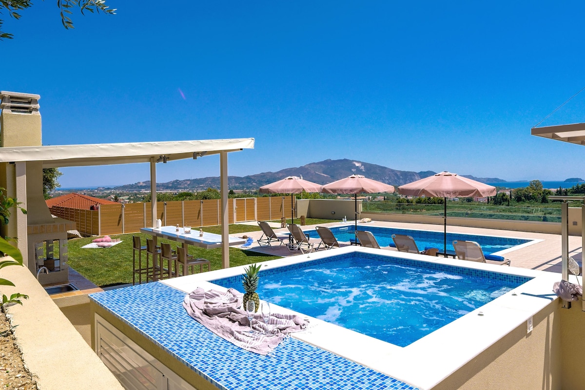 An outdoor space is presented featuring a private pool surrounded by sun loungers. Shade is provided by umbrellas, while a terrace offers a seating area with a view of the surrounding hills and clear blue sky.