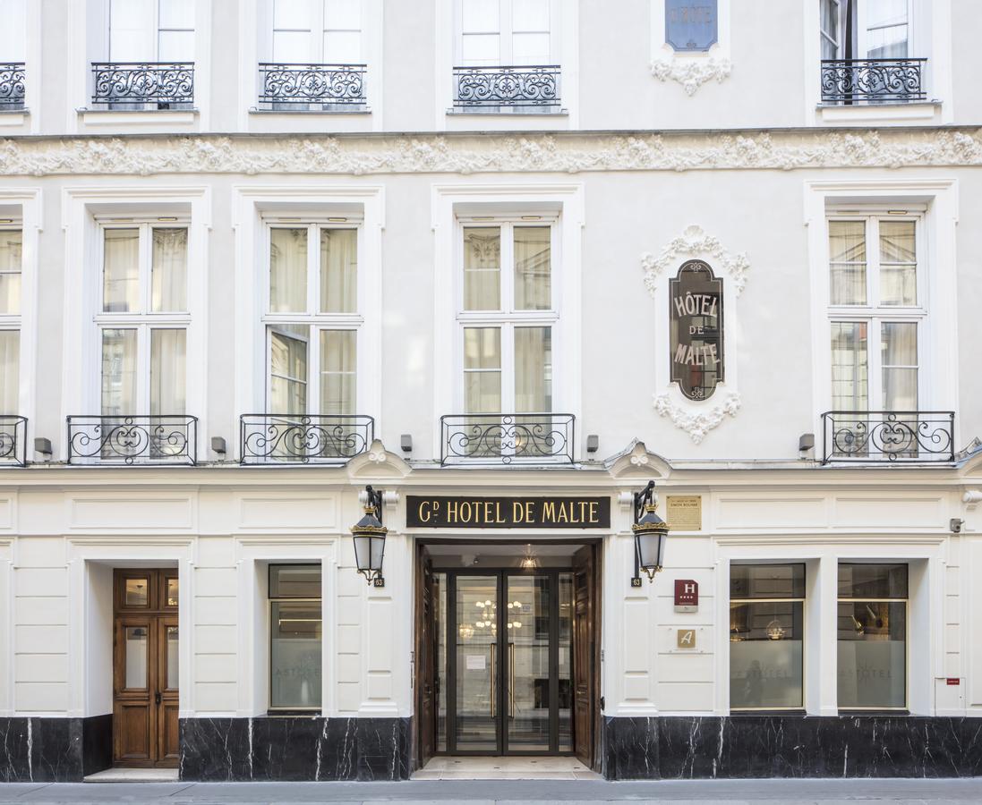 The hotel facade features a classic design with large windows and ornate balcony railings. A welcoming entrance is highlighted by elegant lighting fixtures. The name 'Hôtel de Malte' is displayed prominently above the entrance, inviting guests to enter the boutique hotel.