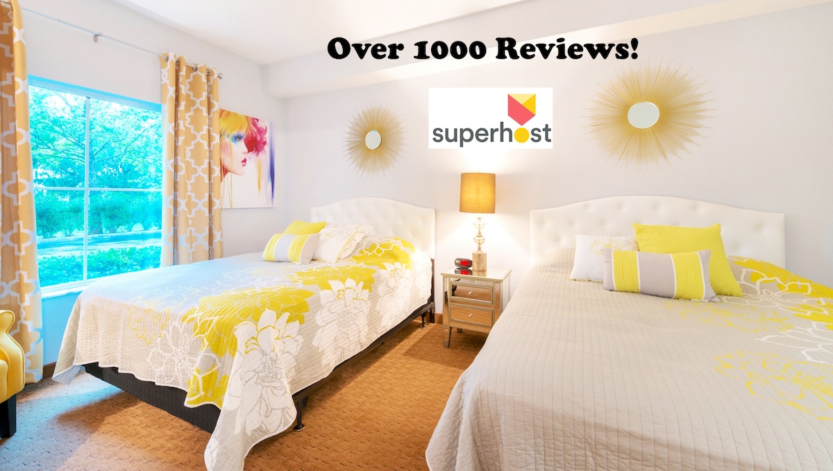 A bright and inviting bedroom features two queen beds adorned with cheerful yellow and white bedding. Large windows allow natural light to fill the space, while decorative curtains enhance the overall ambiance. A nightstand with a lamp adds practical convenience to the room.