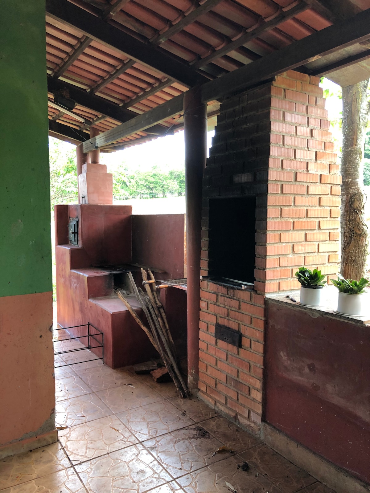 An outdoor cooking area is provided, featuring a traditional barbecue grill constructed from red brick. Adjacent to the grill, a small seating area is visible. Potted plants are placed on a countertop, adding a touch of greenery, while a portion of the roof offers shade.