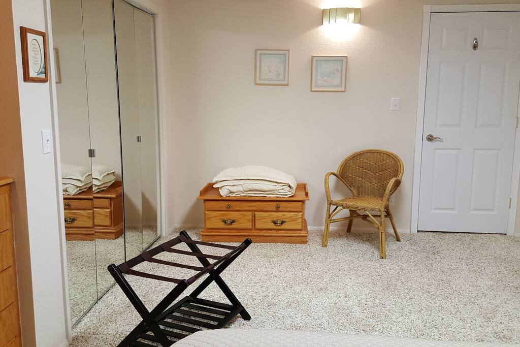 Large closet with mirrored, bi-fold doors, luggage rack, oak blanket chest & chair in bedroom. Door enters kitchen and living room area.
