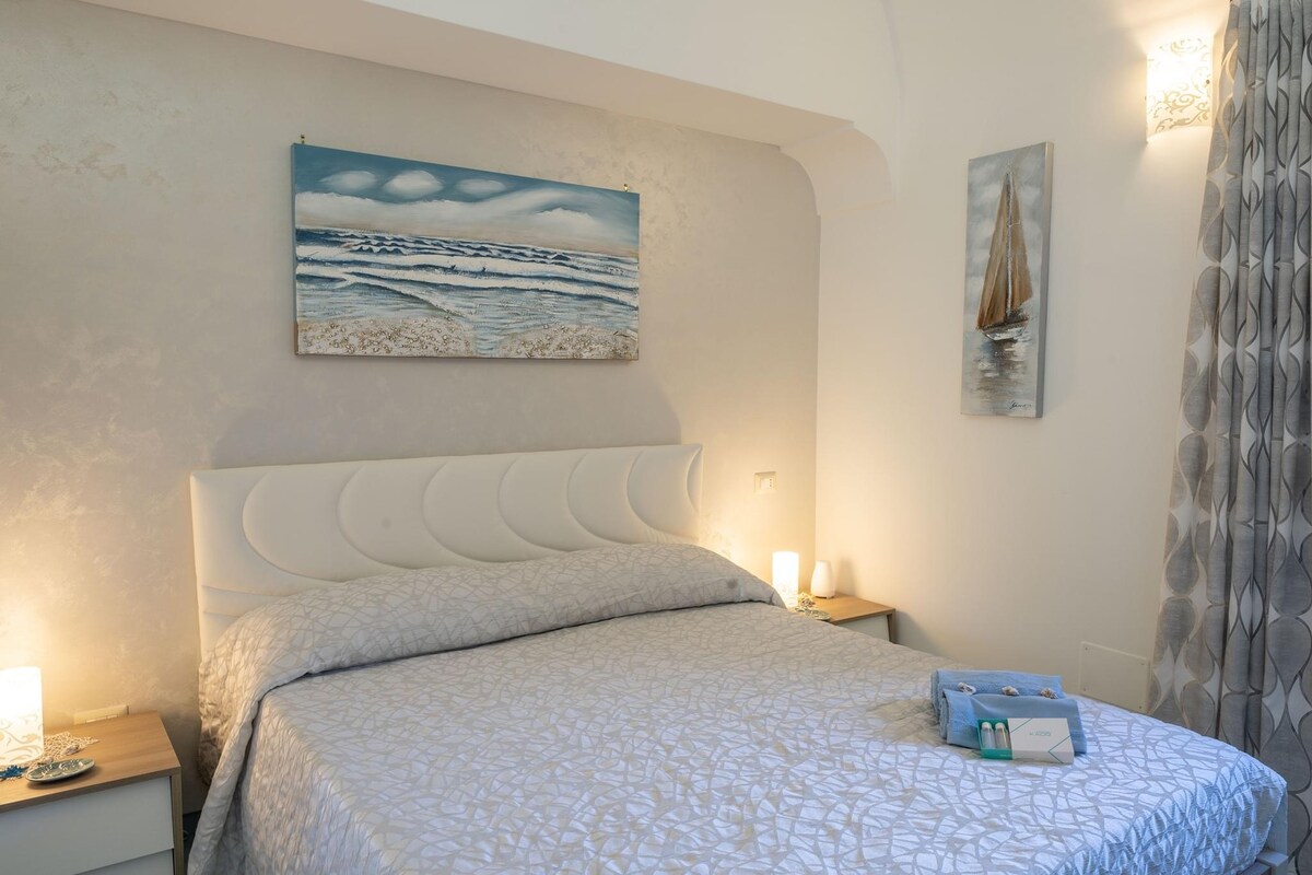 Спална соба со двоен кревет, две ноќни масички со поврзани ноќни ламби и декориран кревет, плус покривки и сапуни што ги има обезбедено конструкцијата за дневната соба.