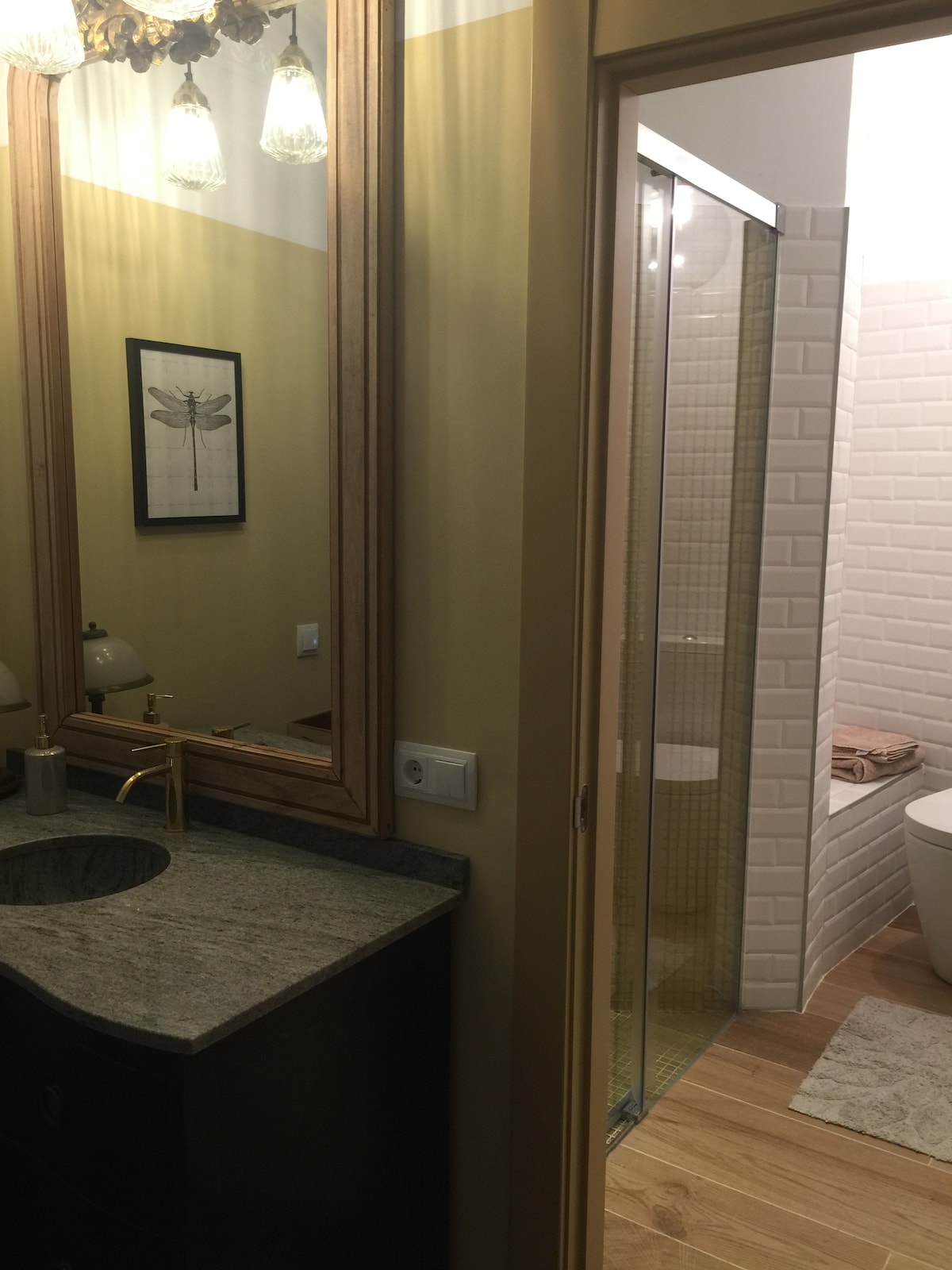 A modern bathroom is featured, showcasing a sleek wooden vanity with a stone countertop. A large wall mirror reflects light from stylish fixtures above. A glass-enclosed shower is visible in the background, along with a minimalist toilet adorned with soft towels.