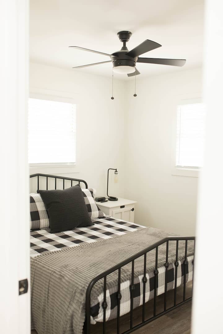This relaxing queen bedroom includes a smart tv, ceiling fan, alarm clock with usb charging capabilities, a closet with hangers and a luggage rack, iron and ironing board, and a full length over the door mirror. 