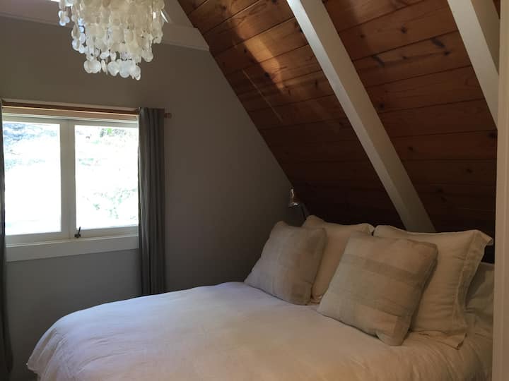 Upstairs master bedroom (queen bed) with organic linens, natural light, new blackout shades, and peaked ceilings