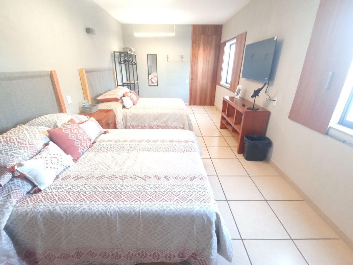 ห้องนอนใหญ่พร้อมเตียงขนาดควีนไซส์ 2 หลังบูโรทีวีพื้นที่เสื้อผ้าและพัดลมแบบพกพา 